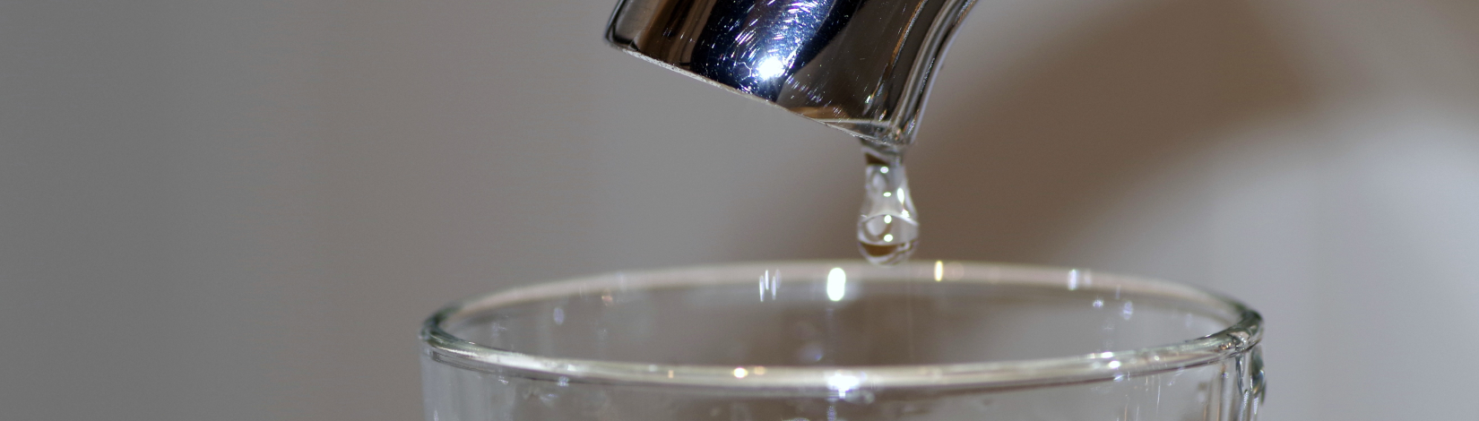 a drop of water falls from a faucet into a waiting glass