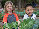 two children smile broadly behind a large, garden plant
