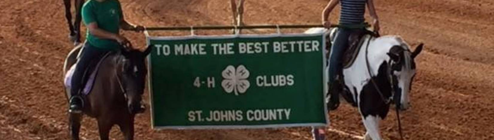 Two youth riding their horses and carrying a 4-H banner at the Area B Horse Show
