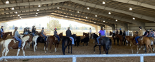 Riders on horseback participate in a training session inside a large indoor arena.
