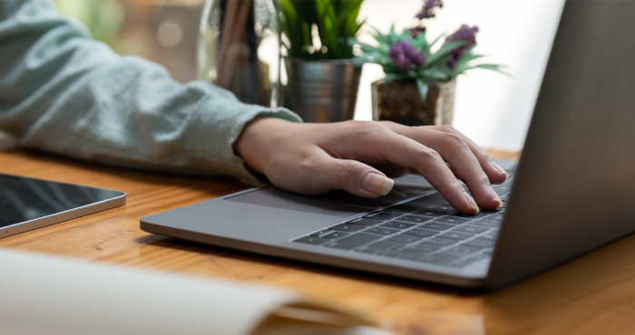 Closeup of a hand typing on a computer in a home office setting.