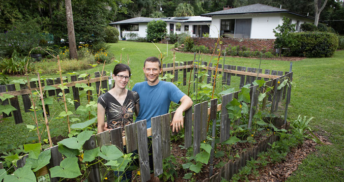 A couple in their backyard victory garden with their home in the background.