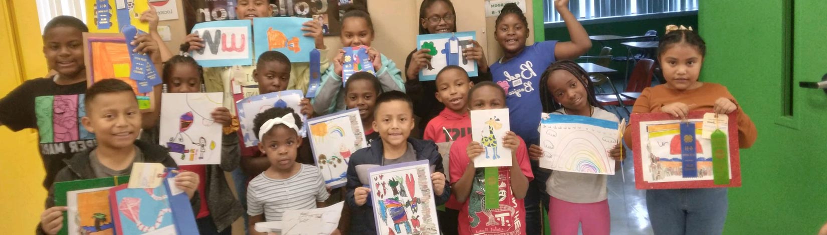 A group of kids at a Bay County after-school program proudly hold up their drawings and ribbons, smiling with excitement.