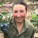 Lauren smiling while holding a blueberry bush.