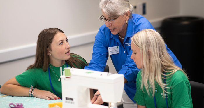A volunteer helping 4-H kids use a sewing machine.