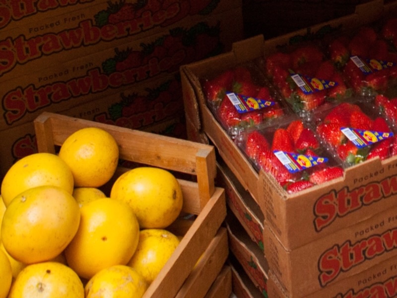 Wooden crate of yellow citrus fruit next to stacked boxes of packaged strawberries.