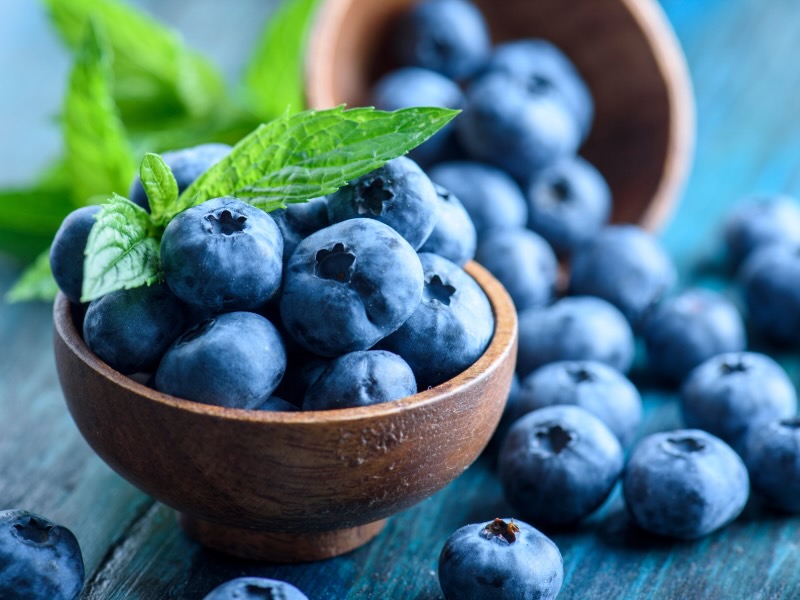Close-up of fresh blueberries in a wooden bowl with sprigs of mint.