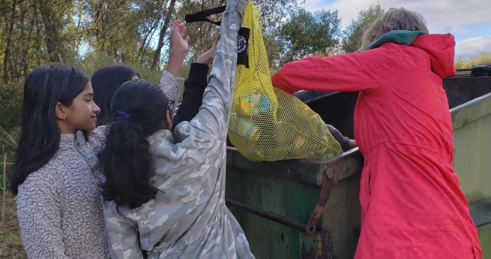 Adult volunteer helping youth throw trash into dumpster