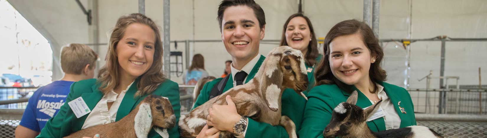 Three 4-H Teens in green suit jackets each holding a baby goat.