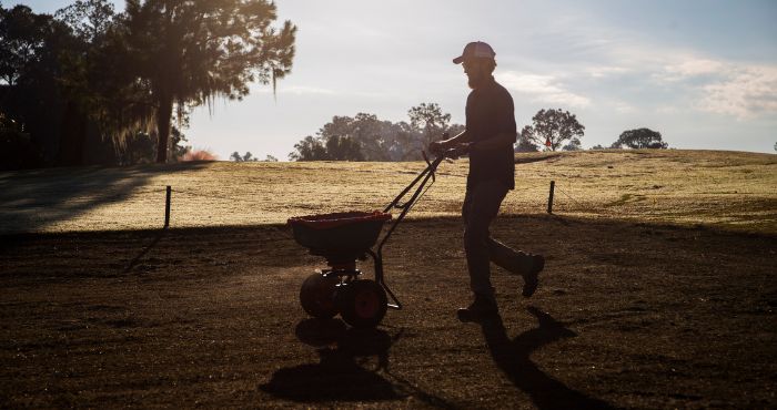 person pushing a fertilizer or pesticide spreader across a grassy field