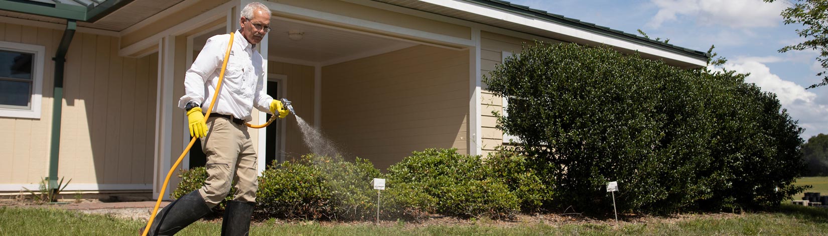 Man in rubber boots spraying pesticides on a lawn.