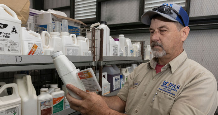 An agent reading the safety and instruction labels of agriculture-based pesticides and fertilizers.