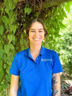 Florida Friendly Extension Agent Heather Kalaman wearing a blue IFAS shirt in front of a plant filled background.