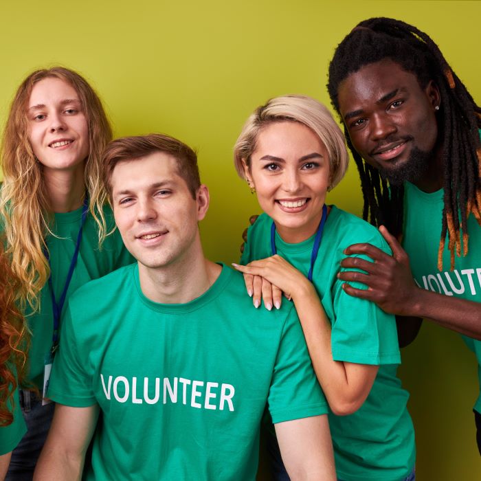 portrait of friendly charity team volunteering together, young altruistic diverse people posing at camera, wearing the same green t-shirts, isolated over green background