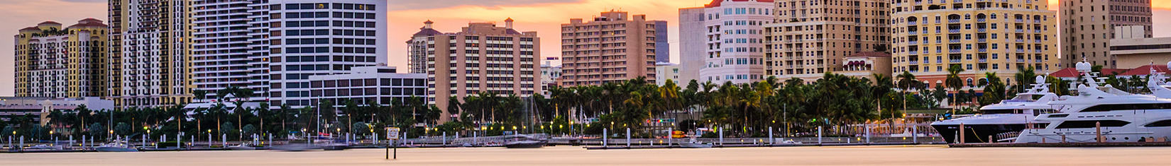 West Palm Beach waterfront at sunset with city buildings in the background and a yacht anchored nearby.