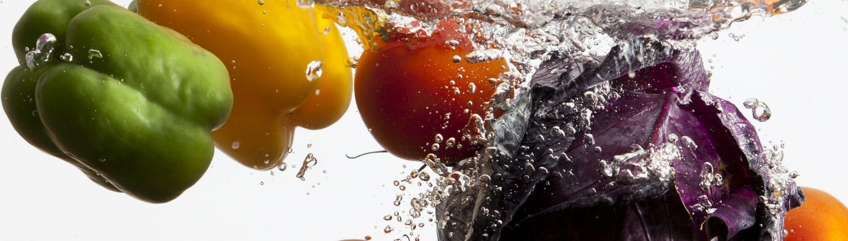Two bell peppers, a tomato, and a red cabbage splash into a clear tank of water. 