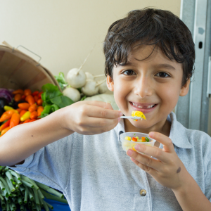 a young boy samples fresh produce from a cup, standing in front of a medley of produce items from an overturned basket. [credit: uf/ifas]