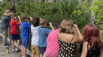 a 4-h agent shows youth how to use binoculars to search for wildlife, with all lined up on a pedestrian bridge looking at a natural area.