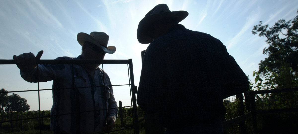 silhouettes of two ranchers working as the sun's light fades