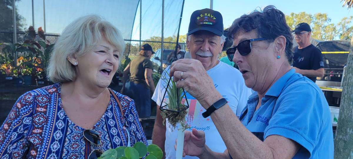 visitors and a master gardener volunteer discuss a tiny plant at the 2022 plant sale and open house