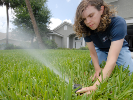 a person kneels and adjusts an irrigation sprinkler spraying water across a grassy area