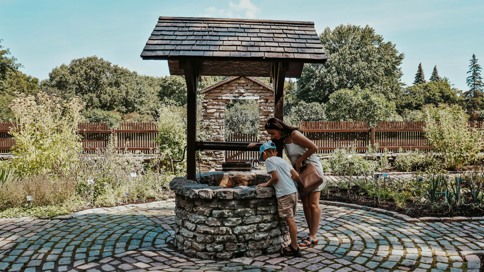 a woman and boy peer into a well, complete with a well structure and roof. [credit: unsplash.com, maxime bouffard]