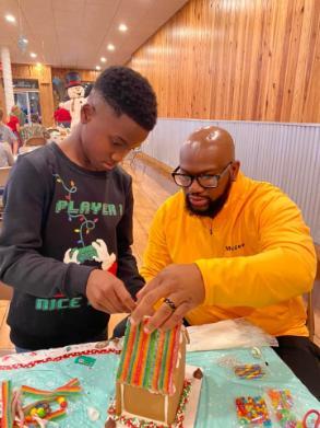 father and son working together to build a gingerbread house. 