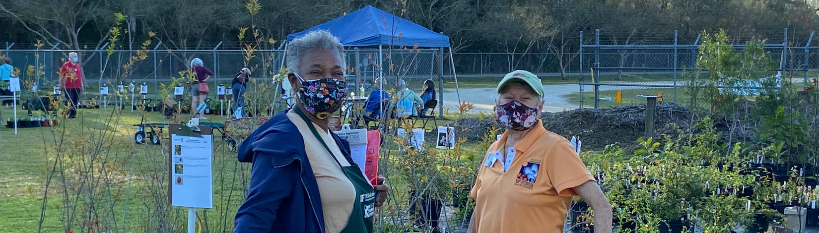 Two Master Gardeners in Masks standing in front of plants